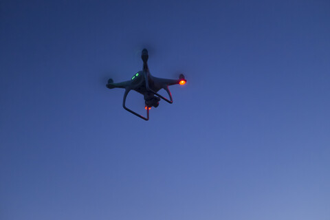 Beleuchtete Flugdrohne mit Kamera gegen Abendhimmel, lizenzfreies Stockfoto
