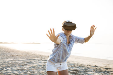 Thailand, woman using virtual reality glasses on the beach in the morning light - HMEF00186