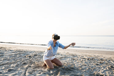 Thailand, woman using virtual reality glasses on the beach in the morning light - HMEF00187