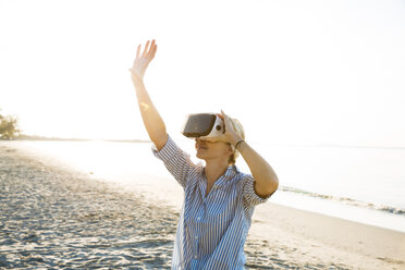 Thailand, woman using virtual reality glasses on the beach in the morning light - HMEF00188