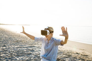 Thailand, Frau mit Virtual-Reality-Brille am Strand im Morgenlicht - HMEF00189