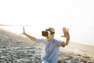 Thailand, woman using virtual reality glasses on the beach in the morning light - HMEF00189