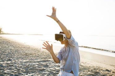 Thailand, woman using virtual reality glasses on the beach in the morning light - HMEF00190