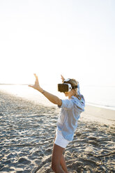 Thailand, woman using virtual reality glasses on the beach in the morning light - HMEF00191
