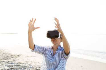 Thailand, woman using virtual reality glasses on the beach in the morning light - HMEF00192