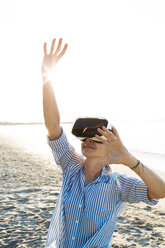 Thailand, woman using virtual reality glasses on the beach in the morning light - HMEF00193