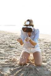 Thailand, woman using virtual reality glasses on the beach in the morning light - HMEF00194