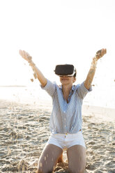Thailand, woman using virtual reality glasses on the beach in the morning light - HMEF00195