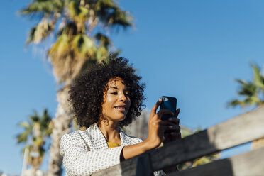 Beautiful woman sitting on a bench in the city, takig pictures with her smartphone - BOYF01318