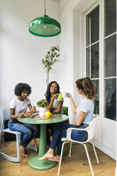 Three happy women sitting at table at home drinking coffee together - GIOF05626