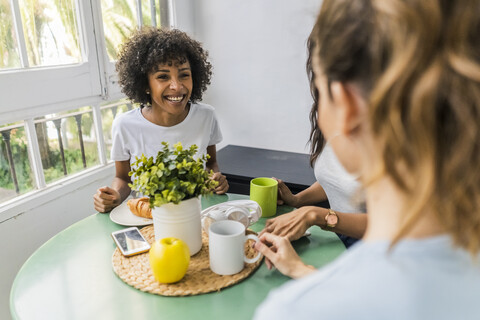 Three happy women sitting at table at home drinking coffee together stock photo