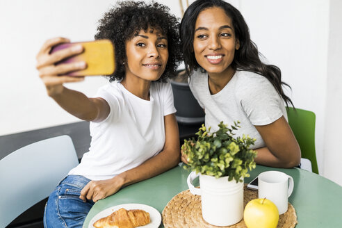 Zwei glückliche Freundinnen sitzen am Tisch und machen ein Selfie - GIOF05629