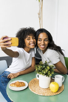 Zwei glückliche Freundinnen sitzen am Tisch und machen ein Selfie - GIOF05630