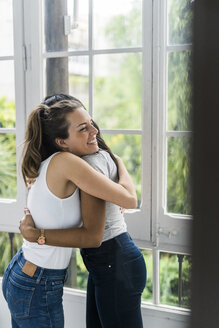 Zwei glückliche Freundinnen umarmen sich am Fenster - GIOF05634