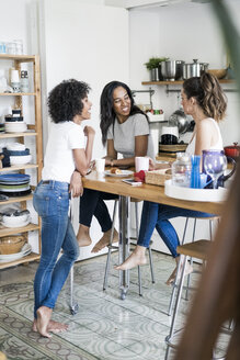 Drei glückliche Frauen beim geselligen Beisammensein am Küchentisch zu Hause - GIOF05644