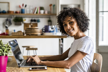 Portrait of smiling woman using laptop at table at home - GIOF05654