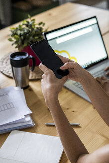 Nahaufnahme einer Frau, die zu Hause am Tisch ein Mobiltelefon benutzt - GIOF05656