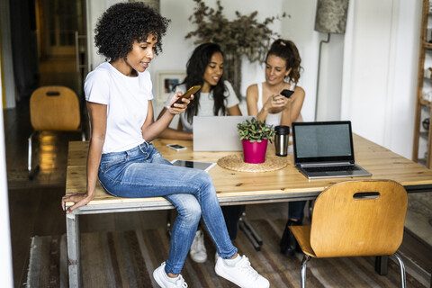 Frau mit Mobiltelefon sitzt auf einem Tisch mit Freunden im Hintergrund, lizenzfreies Stockfoto