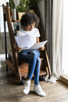 Frau sitzt auf den Stufen zu Hause und betrachtet ein Dokument - GIOF05667