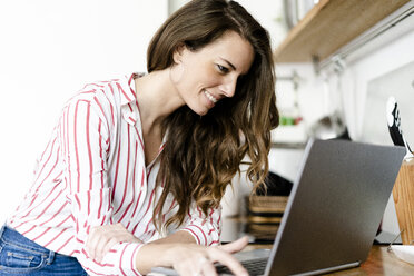 Lächelnde Frau mit Laptop in der Küche zu Hause - GIOF05678
