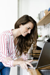 Smiling woman using laptop in kitchen at home - GIOF05679