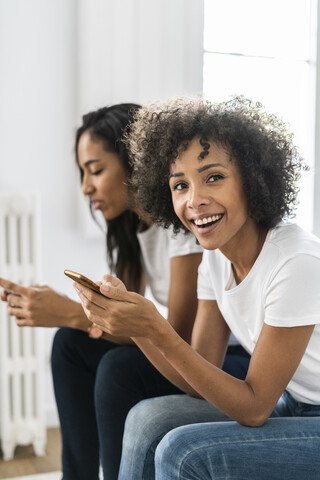 Porträt einer glücklichen Frau zu Hause mit Mobiltelefon, lizenzfreies Stockfoto