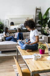 Smiling woman using tablet on table at home with friends in background - GIOF05684