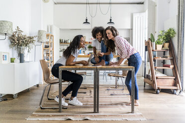 Three happy women with digital devices on table at home - GIOF05688