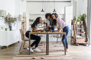 Drei glückliche Frauen mit digitalen Geräten auf dem Tisch zu Hause - GIOF05688
