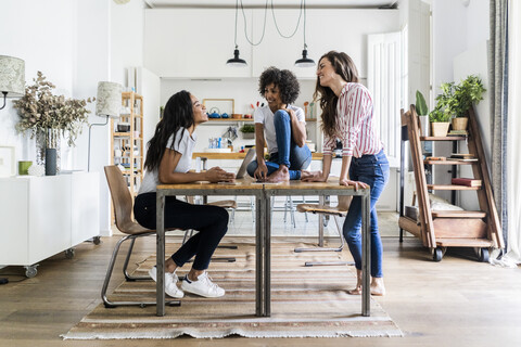 Drei glückliche Frauen unterhalten sich am Tisch zu Hause, lizenzfreies Stockfoto