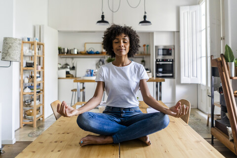 Lächelnde Frau mit geschlossenen Augen in Yoga-Pose auf dem Tisch zu Hause, lizenzfreies Stockfoto