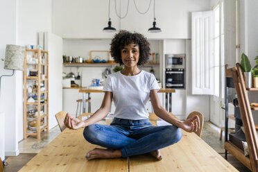 Porträt einer lächelnden Frau in Yoga-Pose auf einem Tisch zu Hause - GIOF05698