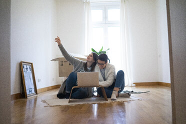 Junge Frauen sitzen auf dem Boden ihrer neuen Wohnung und benutzen einen Laptop - MOEF01933