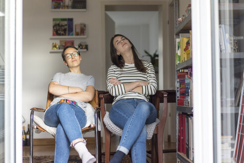 Two girlfriends at home sitting in the kitchem with open door, enjoying the sun - MOEF01953