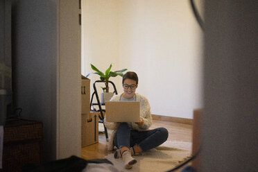 Young woman sitting on floor of her new home, using laptop - MOEF01956