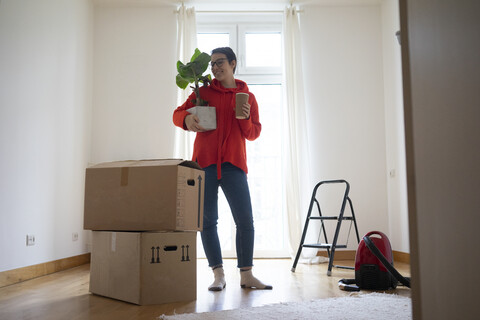 Junge Frau zieht in ihr neues Haus ein und trägt eine Topfpflanze, lizenzfreies Stockfoto