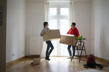 Young women moving into their new home, carrying cardboard boxes - MOEF01976