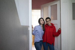 Zwei Freundinnen zu Hause im Türrahmen stehend, die Arme umeinander gelegt - MOEF01979