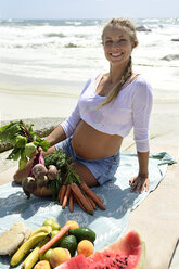 Porträt einer lächelnden schwangeren Frau am Strand mit gesundem Picknick - ECPF00304