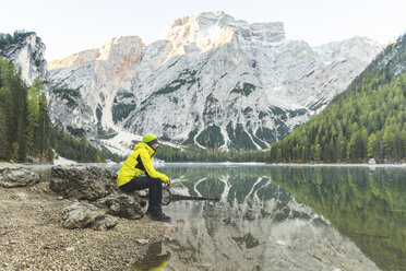 Italien, Pragser Wildsee, Mann sitzt auf einem Felsen am Seeufer mit Bergen und Wald im Hintergrund - WPEF01342