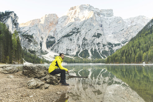 Italien, Pragser Wildsee, Mann sitzt auf einem Felsen am Seeufer mit Bergen und Wald im Hintergrund - WPEF01343