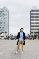 Spain, Barcelona, portrait of smiling man standing in the city with two skyscrapers in the background - JRFF02497