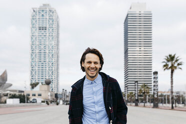 Spain, Barcelona, portrait of laughing man in the city with two skyscrapers in the background - JRFF02498