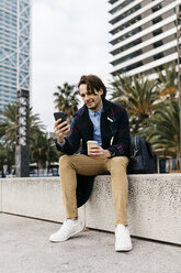 Spanien, Barcelona, Mann sitzt in der Stadt mit Kaffee zum Mitnehmen und Mobiltelefon - JRFF02502