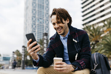 Spanien, Barcelona, glücklicher Mann mit Kaffee zum Mitnehmen und Mobiltelefon in der Stadt - JRFF02503