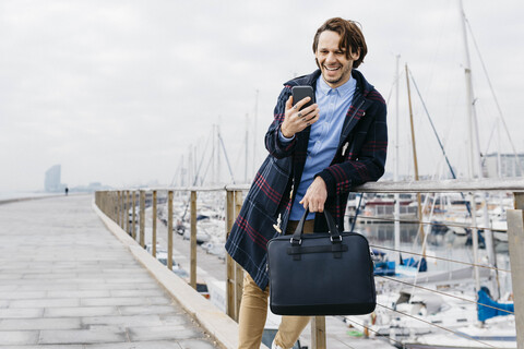 Spanien, Barcelona, glücklicher Mann mit Handy am Hafen, lizenzfreies Stockfoto