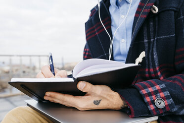 Mann mit einem tätowierten Wifi-Symbol auf der Hand, der draußen sitzt und Notizen macht - JRFF02523