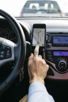 Nahaufnahme eines Mannes mit tätowierter Hand, der ein Auto fährt und ein Mobiltelefon als Navigationssystem benutzt - JRFF02538