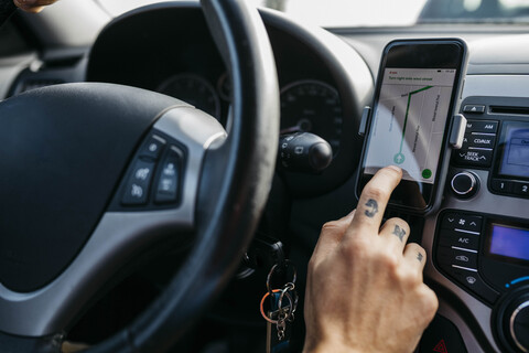 Nahaufnahme eines Mannes mit tätowierter Hand, der ein Auto fährt und ein Mobiltelefon als Navigationssystem benutzt, lizenzfreies Stockfoto