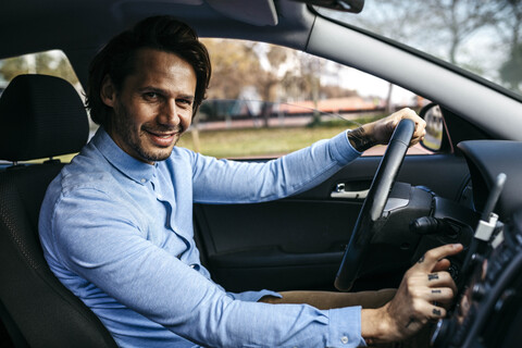 Porträt eines lächelnden Geschäftsmannes, der ein Auto fährt und ein Mobiltelefon als Navigationssystem benutzt, lizenzfreies Stockfoto